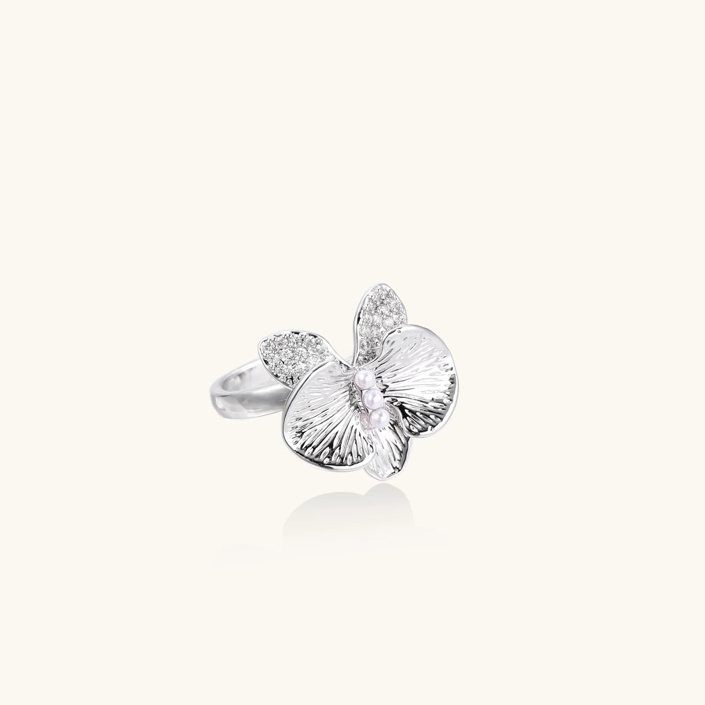 Silver-toned orchid ring with textured petals, pearl center accents, and sparkling zirconia stones on white background.