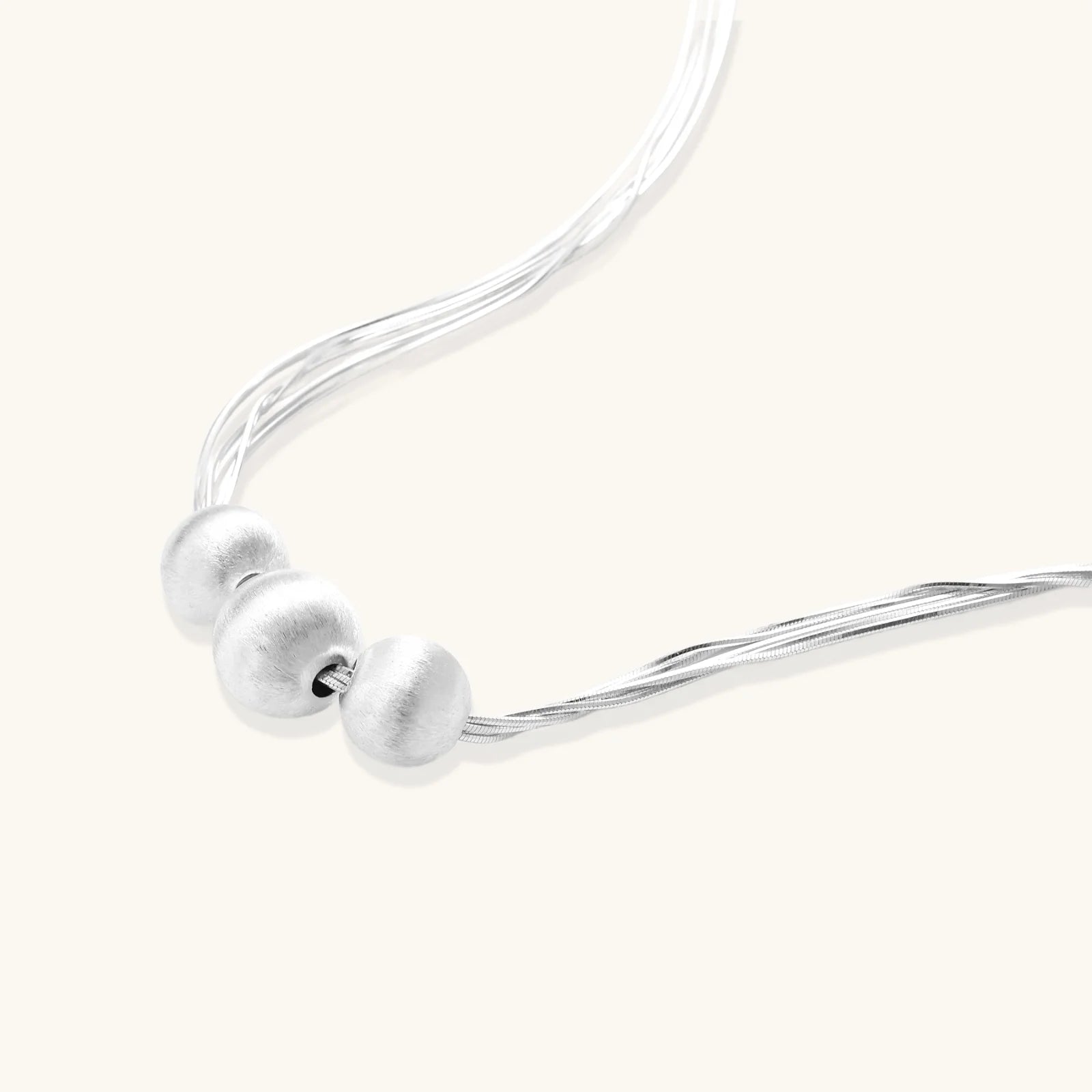 Sterling silver multi-strand necklace with three brushed round beads on cream background