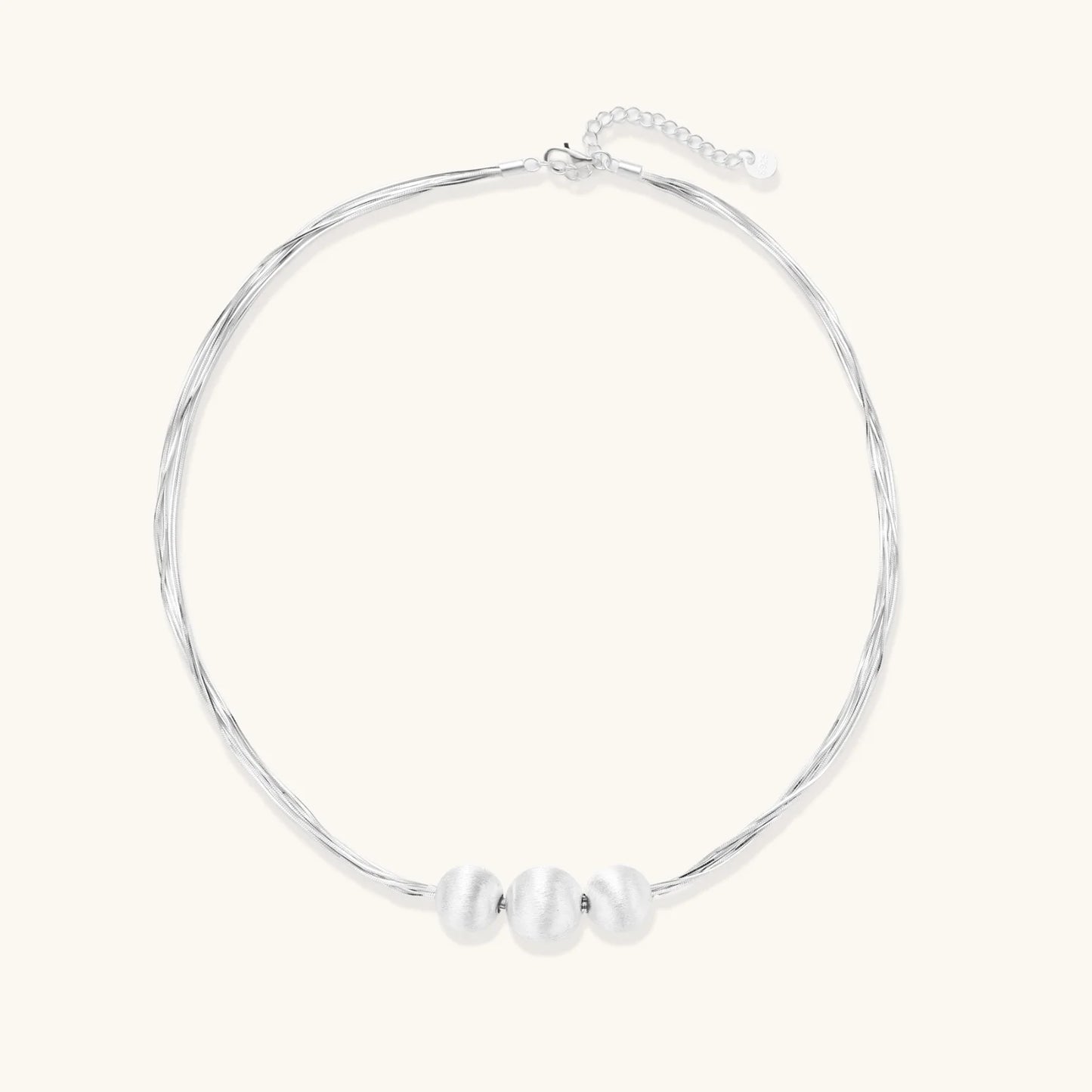 Sterling silver multi-strand necklace with three brushed round beads on cream background